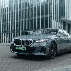 Eleganckie, szare BMW i5 z czarnymi felgami stoi przed nowoczesnym budynkiem biurowym.