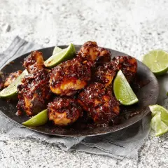En tallrik med krispiga, klibbiga kycklingbitar, garnerad med limeklyftor.