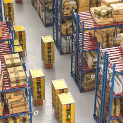 Duże magazynowe zapasy towarów na regałach i paletach. Automatyczne wózki transportują towary między rzędami.