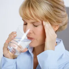 Frau mit Kopfschmerzen trinkt Wasser, hofft auf Linderung durch Magnesium.