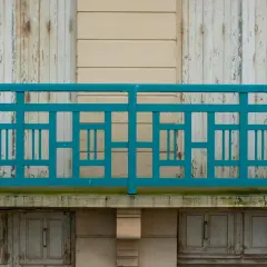 Turkusowe, geometryczne mocowanie balustrady od czoła, z widocznymi odrapanymi drzwiami poniżej.