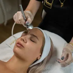 Zabieg dermaoxy na twarz młodej kobiety. Kosmetolog wykonuje zabieg urządzeniem, które rozpyla strumień tlenu i substancji aktywnych.
