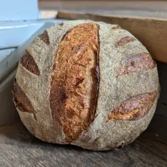 Ein goldbraunes Sauerteigbrot mit markanter Kruste und Einschnitten liegt auf einem Holzbrett. Die Frage "wie lange sauerteigbrot gehen lassen" beschäftigt Bäcker weltweit.