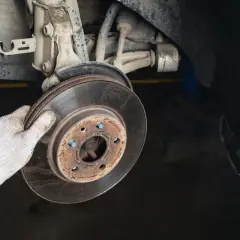Main tenant une pièce rouillée, un disque de frein usé. L'état de cette pièce est crucial pour la durée de vie du disque de frein.