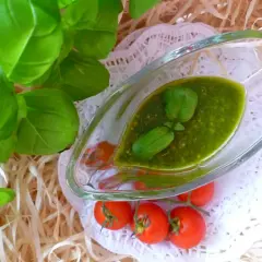 Aromatyczne pesto z bazylii w sosjerce, ozdobione listkami bazylii i pomidorkami koktajlowymi.