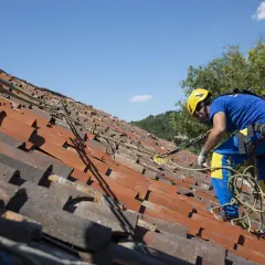 Trabajador con equipo de seguridad en un tejado de tejas rojas, mostrando diferentes tipos de tejados y la importancia de la seguridad.