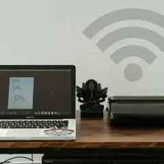 Laptop, drukarka i figurka Ganesha na biurku. Ikona Wi-Fi na ścianie sugeruje, jak połączyć drukarkę z wifi bezprzewodowo.