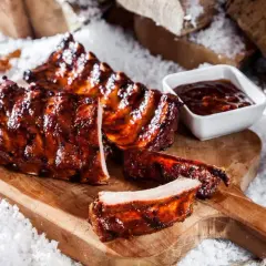 Saftige spareribs im backofen, glasiert und mit BBQ-Sauce, auf einem Holzbrett mit Schnee dekoriert.