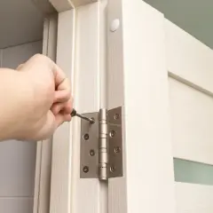 Dłoń dokręca śrubę zawiasu, regulując drzwi zewnętrzne. Trzy zawiasy zapewniają stabilność.
