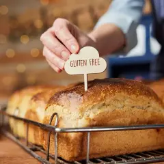 Dłoń wtyka tabliczkę "Gluten Free" w bochenek chleba. To przypomnienie, jak ważne jest, by wiedzieć, co robi gluten w organizmie, zwłaszcza przy wyborze pieczywa.