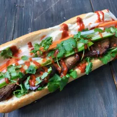 En saftig banh mi med tofu, färska grönsaker och en härlig sås på en träbakgrund.
