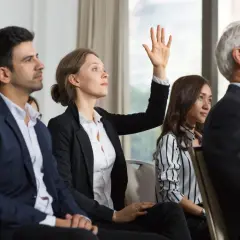 Une femme lève la main lors d'une réunion, posant une question sur le délai entre 2 ag de copropriété.