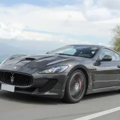 Szary Maserati GranTurismo na krętej drodze. Marzysz o takim aucie? Sprawdź aktualną maserati cena!
