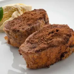 Dos torrijas de chocolate espolvoreadas con cacao y azúcar, acompañadas de helado de vainilla y una hoja de menta.