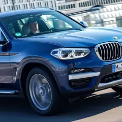Niebieskie BMW X3 w ruchu miejskim. Zastanawiasz się, ile kosztuje BMW X3? Ten model wygląda na nowy i luksusowy.