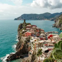Pueblo costero de casas coloridas en un acantilado, con el mar azul y montañas al fondo. Un lugar que evoca la esencia de la spezia el ejido.