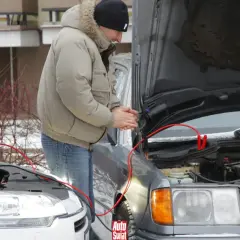 Mężczyzna podłącza kable rozruchowe do silnika samochodu.