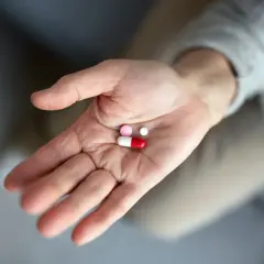 Dłoń trzyma garść tabletek, w tym kapsułkę i dwie mniejsze pigułki. To antybiotyk po wyrwaniu zęba, który pomoże w leczeniu.