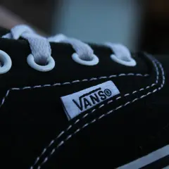 Zbliżenie na czarną tkaninę buta Vans z białymi sznurówkami i charakterystyczną metką.