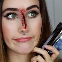 Sista minuten halloween sminkning: ett sår med häftklamrar på näsan, en häftapparat i handen.