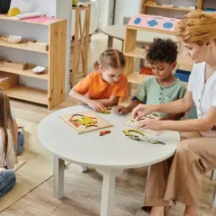 Niños y maestra armando rompecabezas en una mesa. Es normal que los niños se toquen entre ellos mientras aprenden y juegan juntos.