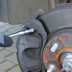 Ręka w rękawicy używa klucza do wymiany klocków hamulcowych w samochodzie.