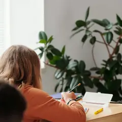 Ein Mädchen konzentriert sich auf seine Aufgaben während der Freiarbeit in der Grundschule. Ein Lehrer steht daneben.