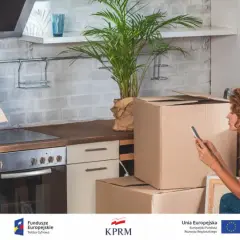 Para urządzająca kuchnię, przygotowująca meldunek tymczasowy. Kartony i rośliny tworzą atmosferę przeprowadzki.