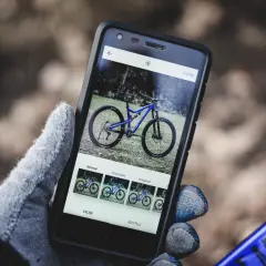 Rękawiczka trzyma smartfon z niebieskim rowerem na ekranie. Aplikacja oferuje filtry, jak w mapach rowerowych.