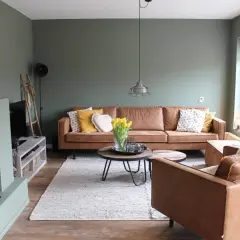 Gemütliches Wohnzimmer mit braunen Ledermöbeln und einer besonderen Wandgestaltung in Salbeigrün. Gelbe Tulpen auf dem Couchtisch.