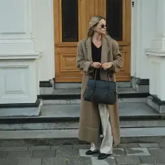 En kvinna med solglasögon bär en elegant brun kappa och håller en stilren vero moda väska.