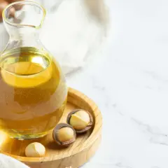 Aceite de macadamia para que sirve: un frasco de vidrio con aceite dorado y nueces de macadamia en un plato de madera.