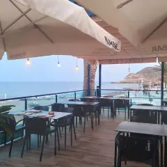 Terraza de restaurante con mesas y sillas, vistas al mar y a la playa. Un lugar ideal para disfrutar de un socorrito las negras al atardecer.