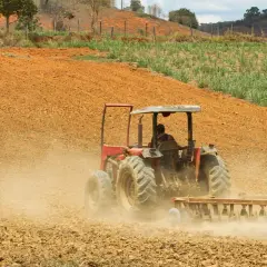 Czerwony traktor z pługiem orze ziemię, wzbijając kurz. To obraz rolnictwa regeneratywnego, przygotowującego glebę do nowego życia.