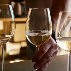 Trzy kieliszki z jasnym winem, jedno z nich trzyma dłoń z obrączką. Degustacja bordeaux wina.