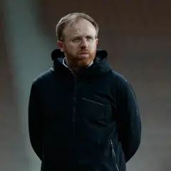 Piotr Stokowiec w czarnej kurtce z kapturem, z okularami i rudą brodą, stoi na tle trybun.