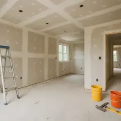 Chantier en cours : murs et plafond en plaques de plâtre, échelle, seaux et outils. Les travaux de second œuvre avancent.