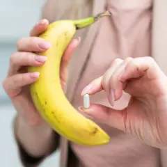 Dłoń trzymająca banana i kapsułkę, sugerującą potas najlepiej przyswajalny z natury i suplementów.