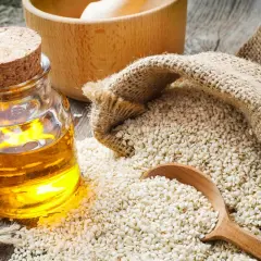 Olio di sesamo dorato in bottiglia, semi di sesamo in un sacco di juta e un cucchiaio di legno. Scopri le incredibili olio di sesamo proprietà.