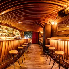Bar de madera con estantes llenos de botellas, taburetes y un techo curvo. ¡Cosas curiosas que ver en Barcelona!