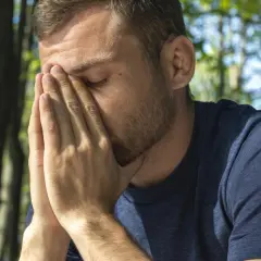 Mężczyzna z dłońmi na twarzy, wyrażający cierpienie. Może to być objaw kaca lub nawet udar alkoholowy.