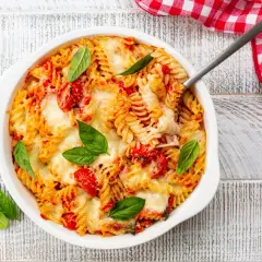 Un plat de pâtes fusilli gratinées avec une sauce tomate savoureuse et du fromage fondant, garni de feuilles de basilic frais.