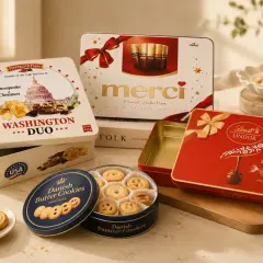 Eleganckie pudełko na ciastka z motywem Waszyngtonu, obok puszki z duńskimi ciasteczkami maślanymi i czerwonego pudełka Lindt.