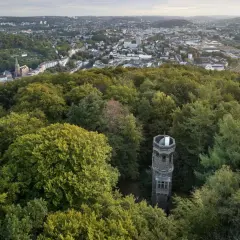 Der von der Heydt Turm ragt aus einem dichten grünen Wald hervor, mit einer Stadt im Hintergrund.
