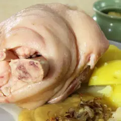 Ein deftiges, gekochtes Eisbein mit Salzkartoffeln, Sauerkraut und einer kleinen Schale mit Soße.