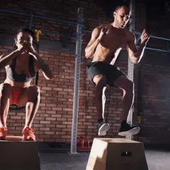 Para i mężczyzna wykonują trening crossfit, skacząc na skrzynie.