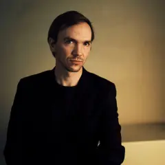 Portret Jana Komasy, reżysera znanych filmów. Jego spojrzenie sugeruje głębię i skupienie, jak w jego kinowych dziełach.