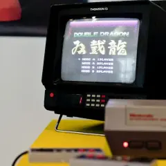 Stary telewizor Thomson z grą Double Dragon. Na ekranie widoczna lista trybów gry, np. "MODE A 1PLAYER". Obok konsola Pegasus.