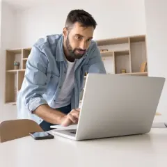 Mężczyzna w dżinsowej koszuli pracuje przy laptopie, analizując swój stosunek pracy.