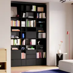 Moderne studio einrichtung mit schwarzem Regal voller Bücher und Deko-Objekte. Ein helles Sofa und ein roter Stehlampen ergänzen den Raum.